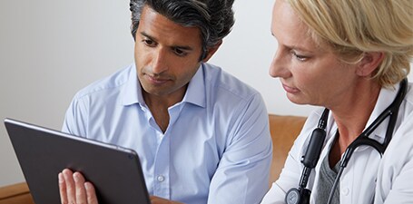 Clinicien auscultant et montrant à l’homme une application sur tablette
